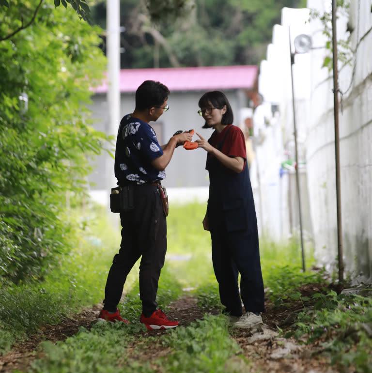 ハウスの間の小道で収穫したブドウを手渡す夫妻