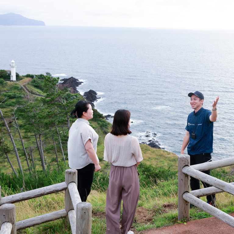 灯台を望む丘で景色を案内する早川さん